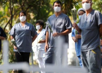 Profissionais de saúde que usam máscaras protetoras seguram flores na frente de cruzes em homenagem à colega de trabalho que morreu em decorrência da covid-19 em São Paulo (Foto: Amanda Perobelli/Reuters)