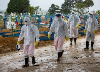 Pessoas usando roupas e equipamentos de proteção contra o coronavírus Sars-CoV-2 andam em meio a túmulos de vítimas da Covid-19 no cemitério Nossa Senhora Aparecida, em Manaus (Foto: Michael Dantas/AFP)
