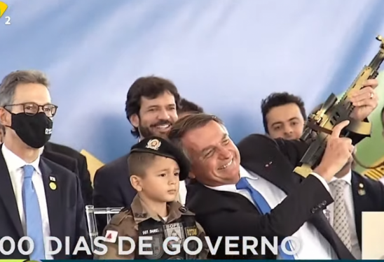 Jair Bolsonaro ergueu uma arma de brinquedo ao lado de uma criança fantasiada com farda da Polícia Militar nesta quinta-feira (30), em Belo Horizonte (MG) (Foto: Reprodução/TV Brasil)