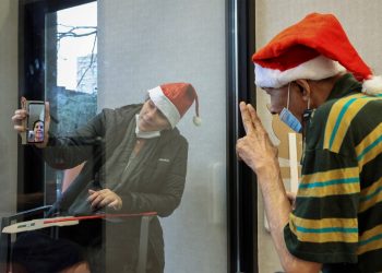 Usando um gorro de Papai Noel, idoso acena para a filha comemorando o Natal através de um vidro de proteção em um centro de enfermagem e reabilitação no bairro do Brooklyn, em Nova York, EUA, com cuidados devidos à pandemia do coronavírus (Foto: Yuki Iwamura/Reuters)